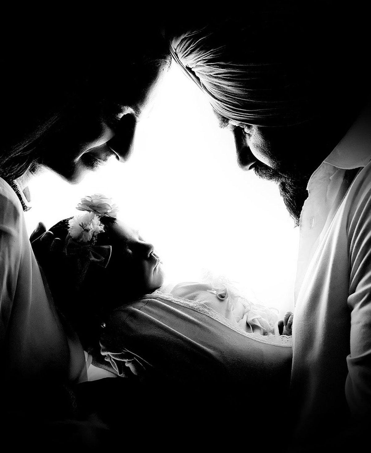 Dramatic black and white newborn photography of parents holding their sleeping baby in beautiful silhouette light