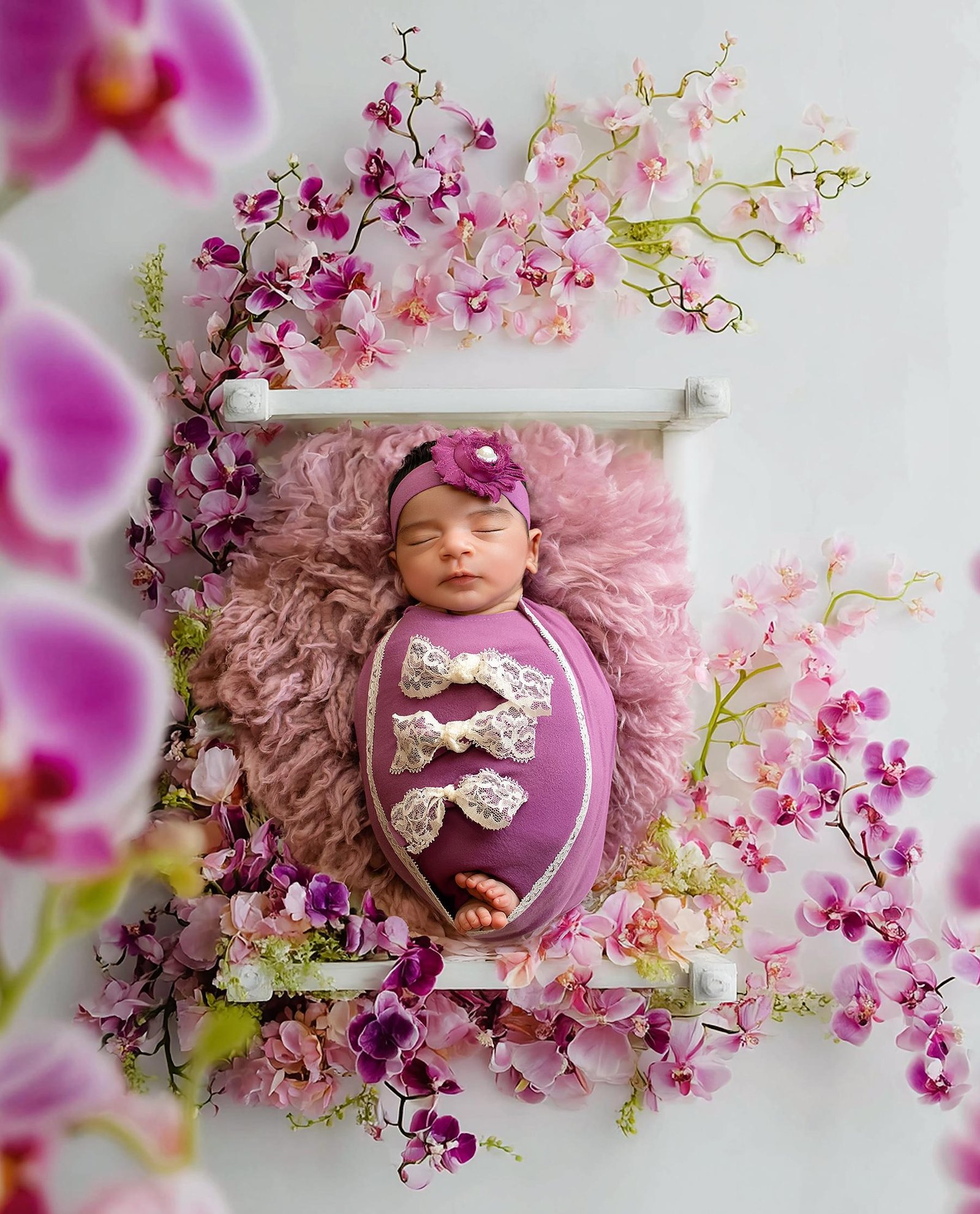 Newborn baby in purple floral setup with delicate flowers – London newborn photographer