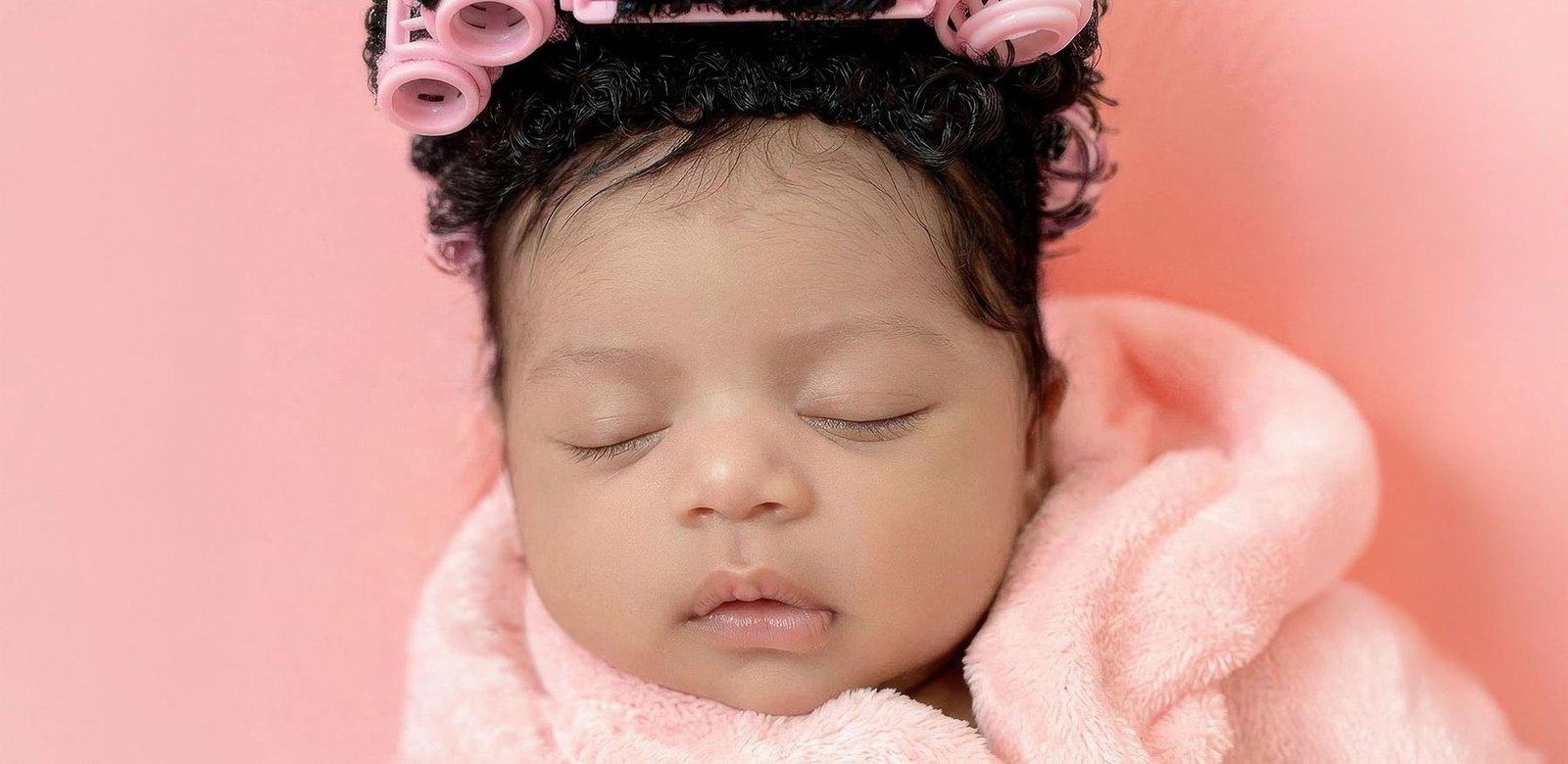 Close-up of newborn baby girl in pink spa setup with curlers and soft tones – London newborn photographer