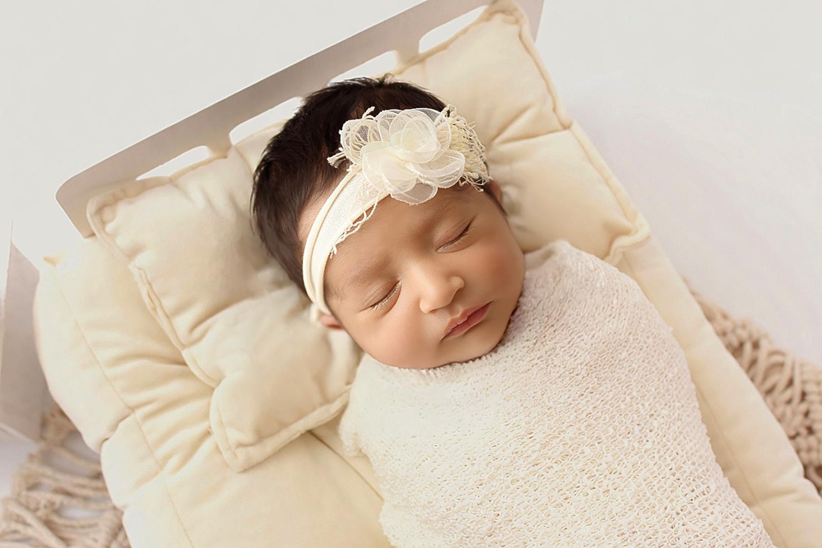 Newborn baby wrapped in cream blanket lying on cushion – London newborn photographer